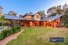 415 Thomas Rd Parkerville WA 6081 $1,600,000 Discover your sanctuary of peace and prestige on this sprawling 9,228 sqm of rural bliss, where natural beauty harmonises with architect-designed sophistication. This extraordinary property boasts a magnificent principal residence paired with a thoughtfully executed one-bedroom self-contained auxiliary living space under the main roof—ideal for guests, multi-generational living, or extended family. 4 bed, 2 bath plus office Stunning architecturally designed Split-level open floorplan Jarrah floors soaring ceilings Multiple living/entertaining Poolside outdoor livings 1 x 2 luxe auxiliary accomm 3-car garage & circle drive 2.28 acre dual entry lot Mains water, pwd w/shop You will fall in love the moment you arrive at this memorable icon of Hills’ design. At the end of a compacted metal driveway, brick paving sweeps towards a grand, porticoed entrance framed by lush landscaping and a central water feature. The connection between nature and the built environment is palpable here, with impressive, large granite steps that anchor the home within its scenic surroundings of native vegetation and granite outcrops. The home’s exterior is striking, with its multi-faceted roofline and a proliferation of angular-shaped, timber-framed windows signalling a lifestyle built on timeless style and luxury. Step inside to be where every detail speaks to consideration for design and craftsmanship. As the front door opens, the warmth of jarrah floors greets you, while bush poles and an inspired use of stone seamlessly blend the indoors with the rugged beauty of the surrounding landscape. Soaring timber-lined ceilings with exposed beams elevate the space, evoking a sense of occasion and grandeur. The multi-level floor plan is a lesson in thoughtful design. The open central living zone is arranged across two levels, creating an intuitive flow that fosters both connection and separation. It is ideally suited to family life and entertaining. The living room, with its striking brick-surround fireplace, invites you to sit, relax, and unwind as the heart of the home embraces you in warmth and comfort. Multiple timber-framed windows capture glimpses of the gardens and grounds and paint patterns of light on the polished timber floors. A few steps down, the dining area and adjoining kitchen await. The kitchen effortlessly blends subtle country styling with modern convenience. The Belfast sink sits alongside modern amenities like a walk-in pantry, a 900 mm electric wall oven, a 4-burner gas hob, a discreet appliance nook, and a dishwasher. From the warm, neutral palette to the carefully considered layout, this space is designed to inspire culinary creativity and serve as the hub of family life. It is where family meals and lively conversations come to life, offering a true sense of home. From the kitchen, a door opens to reveal a versatile, expansive office and adjoining music room, complete with a built-in bar and a powder room for added convenience. This flexible space is designed for creativity and entertainment, ideal for everything from remote work to social gatherings. Adjoining the music room is a large activity room, bathed in natural light, thanks to its vast windows framing garden views. The high timber ceilings, air conditioning, and slow-combustion fireplace perfectly balance rustic charm and modern comfort. French doors open from the activity room onto a verandah and lawn to create an indoor-outdoor entertaining area. The patio and garden provide a serene retreat steps from the below-ground pool and poolside alfresco dining area. Relaxation becomes second nature in this home, and every day feels like a holiday. The principal suite is a sanctuary designed for rest, relaxation, and indulgence. You are welcomed into a large, air-conditioned bedroom infused with an air of serenity. With doors that open directly to the garden, the space feels expansive and intimate, offering a private connection to the outdoors that floods the room with natural light and the tranquil sounds of nature. A generous walk-in robe provides ample storage, while the elegantly appointed bathroom and powder room ensure a sense of luxury and convenience. The thoughtful design allows adjoining rooms to be seamlessly incorporated, transforming the principal suite into a spacious, multi-room haven perfect for parents seeking a quiet escape or a luxurious space to relax, recharge, and reconnect. A stone and timber staircase ascends to the first floor, a space that perfectly balances function and flexibility. The upper level is designed with growing families in mind, with junior bedrooms centred around an air-conditioned activity room. This inviting, versatile space can adapt to any number of needs. Whether it becomes a playroom, a study area, or a cozy spot for movie nights, this ‘bonus’ room is the ultimate hub for creativity, relaxation, or fun. Three junior bedrooms radiate from this central activity zone, each appointed with built-in robes. Two of the bedrooms also feature custom-fitted workstations, ideal for homework, hobbies, or quiet study. The layout of this level is both practical and accommodating, offering children and teens the room to evolve with their ever-changing needs and interests. A shared bathroom and a separate WC complete the first-floor layout. Set under the main roof yet entirely separate from the principal residence, impeccably presented and stylishly finished one-bedroom, one-bathroom secondary accommodation offers a world of possibilities. A source of rental income for the current owners, this versatile space provides an impressive solution for multi-generational living or an independent retreat for guests. Following the split-level design of the main home, the floor plan creates an inviting sense of openness and flow. The central living room and kitchen/meals area are arranged in a seamless open-plan layout, offering a modern, airy space perfect for comfortable living and easy entertaining. The large bedroom with a mezzanine level brings functionality and character to the space. Stepping from the bedroom, you’ll find a private, peaceful backyard. The accommodation also includes a laundry with a second shower and WC. Offering an elevated level of amenity, a spacious, covered courtyard with ample space for outdoor dining, lounging, and entertaining allows for a seamless indoor-outdoor lifestyle that enhances the versatility and appeal of the entire property. Whether as an independent living solution for extended family members or a rental option, this secondary accommodation offers both luxury and flexibility, creating endless possibilities for income or shared living without compromising style or privacy.