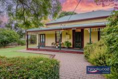 2965 Jacoby St Mundaring WA 6073 $1,000,000 In the heart of Mundaring, where the rhythm of modern life meets Western Australia’s pioneering past, stands a weatherboard and iron cottage that embodies the very essence of heritage living. Built circa 1901 by retired Bunbury harbour master Captain Thomas Scott, the remarkable “Stratheden” carries within its weatherboard walls the pioneering spirit that shaped early Western Australia. Hidden from the street by a charming picket fence and enveloped in lush, established gardens, this remarkable workers’ cottage offers a rare opportunity to inhabit a piece of living history whilst enjoying the unparalleled convenience of one of the region’s most coveted locations. 3 bedrooms 1 bathroom 1901 weatherboard & iron Striking workers’ cottage Extensive Jarrah panelling Wide jarrah floorboards High pressed metal ceilings Rear lane access to garage Estab gardens, bore retic 2023 sqm heart Mundaring Steps to Trail, park, village The extensive use of jarrah throughout this property immediately distinguishes it as a superior example of vernacular architecture, where wide floorboards and striking panelling speak to the craftsmanship and material abundance of a bygone era. Here, the integrity of the original fabric has been meticulously preserved, creating an authentic connection to the past that is increasingly rare. This is not simply a house that has been renovated; it is a heritage treasure that has been lovingly maintained, telling the story of Western Australia’s timber heritage. The approach to the home sets the tone for what lies beyond – a wide, bullnose verandah extends a gracious welcome, while pressed glass in subtle pastel hues surrounds the front door like jewels set within a frame. Living here means beginning each day with this gentle beauty, where morning light filters through coloured glass and the established gardens create a private sanctuary mere steps from Mundaring’s vibrant village centre. Upon crossing the threshold, the significance and integrity of this property become immediately apparent through the soaring ceiling, its pressed metal painted white, creating a striking vertical dimension that speaks to the generous proportions seen throughout the home. Picture rails and wide jarrah floorboards create a striking welcome that sets expectations high, and the home delivers on every promise. The entrance hall is flanked by two generously proportioned bedrooms, each graced with original windows, pressed metal ceilings and decorative fireplaces. At the end of the hallway, a pair of interior doors open to reveal the property’s masterpiece – a living room that embodies an authentic and uniquely Western Australian aesthetic. Vertical jarrah boarding rises to dado height, and horizontal panelling continues to the jarrah-clad ceiling. An expanse of eight-paned windows draws northern light into the heart of the home, creating a space where the seasons become part of daily life, where winter afternoons glow golden against the jewel-toned timber and summer mornings arrive soft and bright. Living in this room means inhabiting a space where craftsmanship and comfort converge, where every surface speaks to the skill of builders who understood both beauty and function. At one corner of this magnificent living space, a breakfast nook provides an intimate setting for morning rituals, whilst the kitchen represents a faultless melding of history and modern convenience. The original chimney breast and hearth, fitted with a Metters stove, anchor the space with authentic period detail, while pressed metal and jarrah panelling blend seamlessly with gold-flecked stone benchtops, under-bench cabinets, and contemporary appliances, including a freestanding electric oven and dishwasher. This kitchen exemplifies how heritage properties can incorporate modern elements without compromising their character. The principal bedroom, accessed via the living room, offers generous proportions. High ceilings ensure an airy, relaxed atmosphere that transforms sleep into restoration, whilst a separate walk-in robe and dressing room provide practical luxury. Reverse cycle air conditioning delivers year-round comfort, demonstrating that while heritage is honoured, contemporary expectations for comfort are uncompromised. Spanning the rear of the plan, a sunroom with a swathe of windows looking out to the rear garden creates a seamless connection between indoor and outdoor living. Terracotta floor tiles ground the space in earthy authenticity, while reverse-cycle air conditioning and direct access to both the rear garden and an alfresco entertaining zone ensure this bright space suits year-round use. A family bathroom and well-appointed laundry at either end of the sunroom complete the thoughtful arrangement of spaces. The transition to outdoor living occurs through French doors that connect the sunroom to a large, crazy-paved patio set beneath a wisteria-threaded pergola – a space where entertaining becomes effortless and where the changing seasons provide an ever-evolving backdrop. Living here means experiencing the joy of alfresco dining where privacy and tranquillity coexist with incredible accessibility to village amenities. The current owner’s dedication as a skilled and passionate gardener has created botanical magic that transforms this property from merely impressive to utterly enchanting. Bore reticulated lawns and gardens cocoon the outdoor living spaces, creating profound privacy and calm despite the home’s remarkably central location. Camellia, deciduous trees, and hardy native plants create a tapestry of colour, texture, and seasonal interest that rewards close observation and daily enjoyment. Practical considerations have not been overlooked – rear lane access leads to a powered garage and a remarkable railway carriage studio, a two-room space complete with verandah that offers endless possibilities for creative pursuits, home business ventures, or simply a peaceful retreat. A small garden shed and single carport enhance the home’s practical amenities. The location represents perhaps the property’s greatest triumph – positioned mere steps from the Sculpture Park and Heritage Trail, with the shops and services of Mundaring Village within comfortable walking distance. Schools, sporting facilities, and public transport networks are all within easy reach of this hidden oasis, creating a lifestyle where convenience never requires compromise of character or tranquillity. Living here means enjoying the best of both worlds: the peace of established gardens and heritage architecture, paired with the vibrancy and accessibility of one of the Hills’ most desirable communities. True luxury lies in authenticity, craftsmanship and connection to place. Here, in this superior example of vernacular architecture, surrounded by a mature garden landscape and positioned in Mundaring’s coveted heart, the past and present converge to create something genuinely extraordinary.