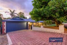 9 Gannon Glen Mundaring WA 6073 $1,399,999 Set beneath the generous canopy of a mature tree, this family home demonstrates how considered design can accommodate the evolving rhythms of domestic life. The architecture employs a disciplined material palette – blackbutt and ceramic tile flooring, soft greys and whites across walls and high ceilings, modern neutrals in the Matrix kitchen – to create a coherent spatial narrative that balances formality with ease in an accessible, adaptable design. 4 bed 2 bath and study 2000-built Guardian home Central open plan design Formal lounge & dining Expansive principal suite Resort-style alfresco & Spa 9m x 18m workshop 5kW solar & auto retic 2003 sqm landscaped block East-facing verandah The plan is organised around a central open-plan living zone, with formal and informal spaces at its heart and a clear separation of private realms: junior bedrooms occupy one wing, the principal suite the other. This zoning extends outdoors, where the interior flows seamlessly to an alfresco area beneath a timber-lined gable roof. The approach is through a terraced front garden enclosed by low fencing. An east-facing verandah leads to the entry, where double doors open onto a tiled foyer. Blackbutt floors define the formal lounge and dining rooms, continuing through to a home office with wraparound desk – positioned to overlook the private rear garden – and into the northern wing’s principal suite. Dual-aspect glazing draws natural light deep into the formal spaces, amplifying the restrained tonal palette. A sliding door reveals the home’s central living zone: a light-filled kitchen, meals and activity area beneath high ceilings, detailed with wainscoting and serviced by split and ducted air conditioning. A slow-combustion fireplace anchors the space. Porcelain tiles flow across the kitchen and meals area, giving way to carpet in a panelled TV room that opens to the east-facing verandah – an ideal spot for morning coffee. The kitchen is finished in soft mushroom cabinetry with Caesarstone benchtops that echo this neutral tone. Appliances include a new steam oven, an electric cooktop and a dishwasher. A bay window frames views to the outdoor entertaining area, accessible through double doors that open to an alfresco zone, spa and a timber-decked gazebo around a central lawn. The junior wing demonstrates a restrained approach to material and colour. White walls and grey tones establish a calm atmosphere across three carpeted bedrooms, each with built-in storage. The bathroom is fitted to spa standard, with a soaking tub, walk-in shower and brass tapware. Even the laundry – equipped with fitted washer and dryer – has been considered as part of the home’s coherent aesthetic. At the northern end, the principal suite comprises a bedroom with blackbutt flooring, a generous ensuite with an accessible shower and a separate WC, and a fitted walk-in wardrobe. A sliding door opens directly onto a private paved patio – a secluded outdoor room screened from view. External stairs descend to a substantial 9m x 18m workshop at the rear, a separate storage room and a high-clearance carport. Accessed via a side driveway, the space is configured for workshop use or secure storage of larger vehicles. A ramp allows for step-free access to the gardens and shed. The property combines well-proportioned living areas, both formal and relaxed, with considered outdoor spaces for entertaining and retreat. A timber-framed workshop, automatic reticulation and 5kW solar array add practical value. High-specification finishes throughout reflect an attention to detail that extends from material selection to presentation. Minutes from the heart of Mundaring, within walking distance of schools and ideally situated for weekends spent exploring the trails and sights of the Perth Hills, this family home accommodates the full spectrum of domestic life.
