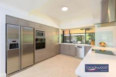 9 Gannon Glen Mundaring WA 6073 $1,399,999 Set beneath the generous canopy of a mature tree, this family home demonstrates how considered design can accommodate the evolving rhythms of domestic life. The architecture employs a disciplined material palette – blackbutt and ceramic tile flooring, soft greys and whites across walls and high ceilings, modern neutrals in the Matrix kitchen – to create a coherent spatial narrative that balances formality with ease in an accessible, adaptable design. 4 bed 2 bath and study 2000-built Guardian home Central open plan design Formal lounge & dining Expansive principal suite Resort-style alfresco & Spa 9m x 18m workshop 5kW solar & auto retic 2003 sqm landscaped block East-facing verandah The plan is organised around a central open-plan living zone, with formal and informal spaces at its heart and a clear separation of private realms: junior bedrooms occupy one wing, the principal suite the other. This zoning extends outdoors, where the interior flows seamlessly to an alfresco area beneath a timber-lined gable roof. The approach is through a terraced front garden enclosed by low fencing. An east-facing verandah leads to the entry, where double doors open onto a tiled foyer. Blackbutt floors define the formal lounge and dining rooms, continuing through to a home office with wraparound desk – positioned to overlook the private rear garden – and into the northern wing’s principal suite. Dual-aspect glazing draws natural light deep into the formal spaces, amplifying the restrained tonal palette. A sliding door reveals the home’s central living zone: a light-filled kitchen, meals and activity area beneath high ceilings, detailed with wainscoting and serviced by split and ducted air conditioning. A slow-combustion fireplace anchors the space. Porcelain tiles flow across the kitchen and meals area, giving way to carpet in a panelled TV room that opens to the east-facing verandah – an ideal spot for morning coffee. The kitchen is finished in soft mushroom cabinetry with Caesarstone benchtops that echo this neutral tone. Appliances include a new steam oven, an electric cooktop and a dishwasher. A bay window frames views to the outdoor entertaining area, accessible through double doors that open to an alfresco zone, spa and a timber-decked gazebo around a central lawn. The junior wing demonstrates a restrained approach to material and colour. White walls and grey tones establish a calm atmosphere across three carpeted bedrooms, each with built-in storage. The bathroom is fitted to spa standard, with a soaking tub, walk-in shower and brass tapware. Even the laundry – equipped with fitted washer and dryer – has been considered as part of the home’s coherent aesthetic. At the northern end, the principal suite comprises a bedroom with blackbutt flooring, a generous ensuite with an accessible shower and a separate WC, and a fitted walk-in wardrobe. A sliding door opens directly onto a private paved patio – a secluded outdoor room screened from view. External stairs descend to a substantial 9m x 18m workshop at the rear, a separate storage room and a high-clearance carport. Accessed via a side driveway, the space is configured for workshop use or secure storage of larger vehicles. A ramp allows for step-free access to the gardens and shed. The property combines well-proportioned living areas, both formal and relaxed, with considered outdoor spaces for entertaining and retreat. A timber-framed workshop, automatic reticulation and 5kW solar array add practical value. High-specification finishes throughout reflect an attention to detail that extends from material selection to presentation. Minutes from the heart of Mundaring, within walking distance of schools and ideally situated for weekends spent exploring the trails and sights of the Perth Hills, this family home accommodates the full spectrum of domestic life.