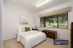 3 Tee Ave Mundaring WA 6073 $850,000 A rare chance to claim almost an acre of established gardens in the heart of Mundaring village, where towering gums and mature plantings create a private world just moments from cafes, shops and schools. 3 beds 1 bath 2 WCs 1994 cedar and iron Airy open floor plan Formal dining room OP kitchen lounge Wrap deck verandah Big under croft space Scheme water & retic 3693 sqm hidden lot Magic in Mundaring The sense of arrival here is immediate. A long driveway moves through layered gardens before delivering you to a cedar home that seems to float among the trees. This is proper privacy – the kind that makes you forget the village centre is just a five-minute walk away. You could be deep in the hills, yet the bakery, supermarkets and coffee are all within easy reach. The home presents a straightforward floor plan that works well for daily life. A central hallway provides clear separation between living spaces and the bedroom wing, with the formal dining room occupying an elevated corner position that places you in the canopy. Morning light filters through established trees, and the room feels more treehouse than traditional dining space. The kitchen is practical rather than showy, fitted with a freestanding oven, dishwasher and a servery window that maintains connection to the dining room. From the carpeted lounge room, a sliding door opens to the front deck – a generous space that becomes an extension of the living area in the warmer months. The reverse-cycle air conditioning handles summer heat, while the mature trees provide natural cooling and the dappled shade that makes outdoor living enticing. The bedroom wing is sensibly arranged. Two bedrooms share the family bathroom, with the current principal bedroom benefiting from split system air conditioning and a ceiling fan. The adjoining powder room can also be accessed via the deck, a detail that proves its worth when you’re entertaining or working in the garden. The first bedroom connects to a spacious storeroom with a dropped floor – a ready-made opportunity for conversion to a second bathroom if that suits your needs. A walk-through laundry with a separate toilet completes this section of the home, and those two double linen presses in the hallway solve the eternal storage question. But step outside, and the real story unfolds. Almost 3,700 square metres of gardens wrap around the house in layers – a mix of native eucalypts, established exotics, fruit trees and the remnants of structured garden beds. The bones are excellent. This was clearly a considered landscape in its day, and while it needs attention now, the framework remains. You can see the potential garden rooms, imagine the restored vegetable beds, picture the fruit trees producing again. The reticulation system is already in place for sections of the garden, and scheme water is connected. This is the kind of property where children create elaborate games among the trees, where you spend weekends gradually bringing order to the wilder sections, and where the undercover area beneath the house suggests possibilities for a workshop or studio space. Friends arrive for lunch and stay until evening, drawn by the atmosphere of seclusion and the novelty of finding such expansive grounds so close to everything. The location delivers genuine convenience – walking distance to the village means less time in the car and more time at home. Mundaring Primary School sits nearby, with Parkerville Steiner schools or Helena College for secondary education. Midland is a 20-minute drive for major shopping and services, the airport is 35 minutes away, and Perth CBD is accessible in around 45 minutes. Yet the property feels entirely removed from the chaos of suburbia.
